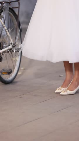 : White dress is lifted and bride shows off her beautiful bridal shoes. Elegant white sandals that complete stylish wedding outfit. Well dressed bride is ready for romantic wedding ceremony.