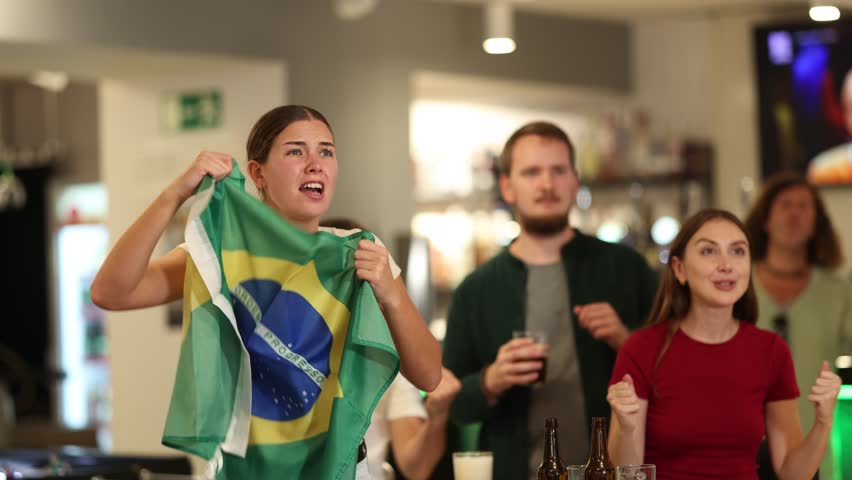 Brazilian fans with the national flag watch the match on TV and express various emotions. High quality 4k footage