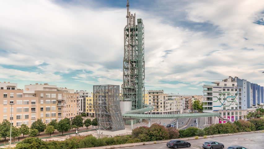 Timelapse hyperlapse of old steel refinery tower with spiral ramp in Lisbon's Park of Nations modern district. Traffic and cloudy sky in the background. Apartment buildings around. Portugal