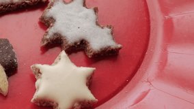 A left-to-right pan of Christmas-themed German Butterplätzchen on a red plate, featuring cookies shaped as trees, stars, and a shooting star, some with white icing for a festive touch - Powered by Shutterstock - Get 15% off with code: PIKWIZARD15