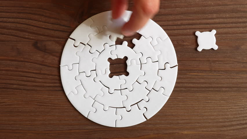 Close-up of a hand inserting puzzle pieces into a circular puzzle design one by one on a wooden table, illustrating problem-solving and cognitive engagement.