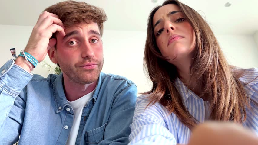A young couple sits indoors on a comfortable sofa during their leisure time, appearing slightly frustrated and bored as they attempt to navigate an app and input a forgotten password