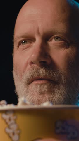 Senior man watching a funny comedy movie at the cinema, he is laughing and eating popcorn