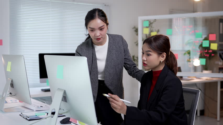 Manager showing a computer screen to an employee in a modern office, facilitating communication and collaboration