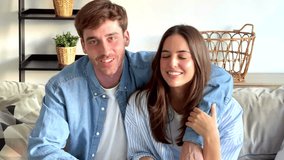 Happy Couple sitting together on a sofa at home in the evening, smiling and chatting with friends or family through a video call using their laptop, seen from the perspective of the camera - Powered by Shutterstock - Get 15% off with code: PIKWIZARD15