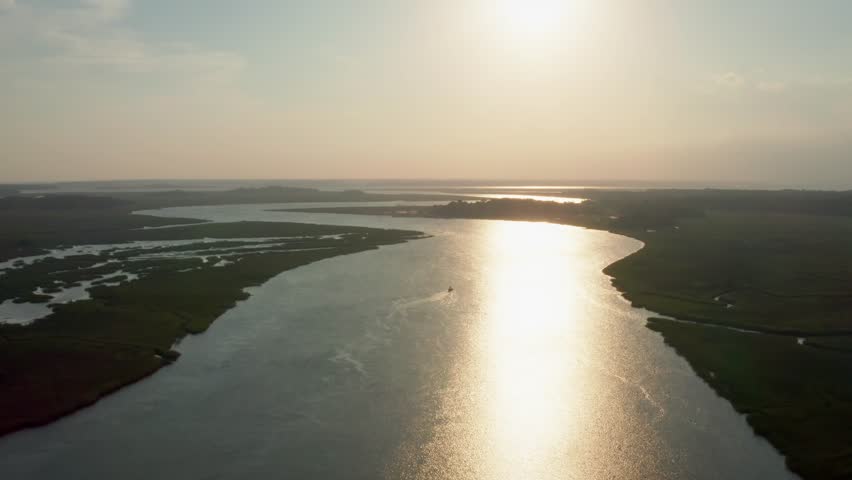 A drone pushes in over marshlands during a glowing sunset at Seabrook Island, South Carolina, capturing a boat gliding across reflective waters.