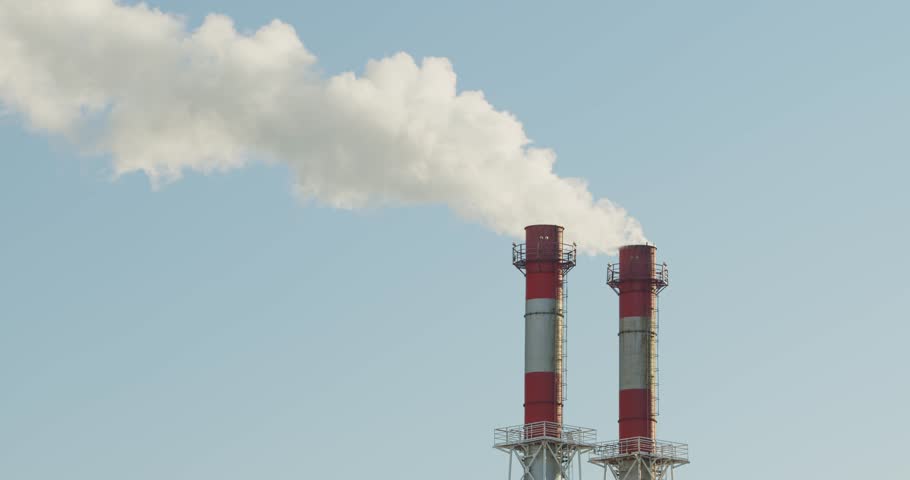 High industrial smokestacks are emitting vapor into the atmosphere against a clear blue sky