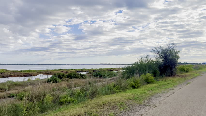 Ride on the Scenic Cycling Path Along the Méjean Pond with Serene Wetland Views and Dramatic Cloudy Sky