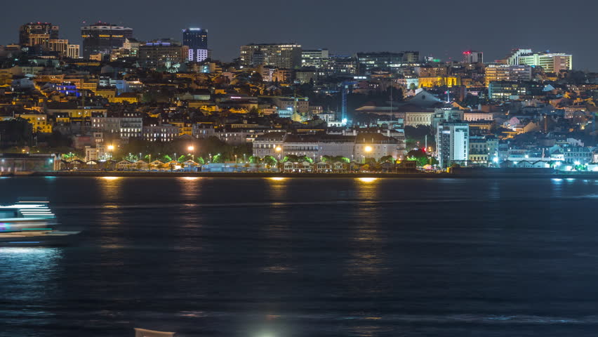 Aerial night timelapse of Lisbon skyline with illuminated Amoreiras towers, Santos district, historic docks and Tagus River viewed from Almada on the southern margin, Portugal