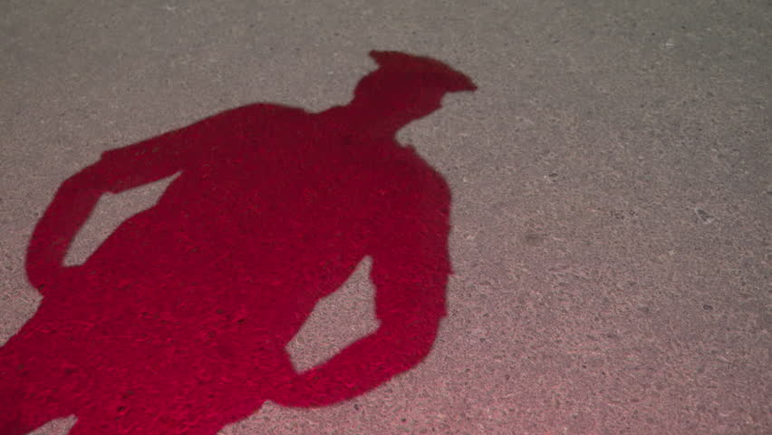 Silhouette of a male cop or police officer stepping in and standing with hands on his waist and looking side to side. View of pavement or road. Policeman checking crime scene, Flashing police lights