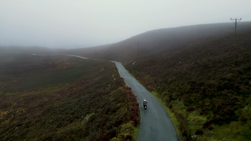 a motorbike rider riding in a mountain wet road during a rainy winter day - Wicklow Mountains - Ireland