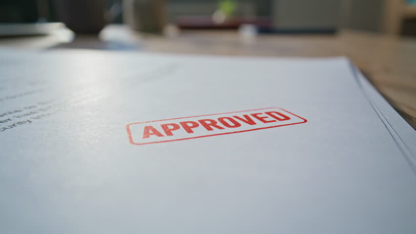 Closeup legal document stamped by unknown lawyer hand in professional office environment. Businessman processing paperwork for contract agreement. Notary approving official documentation at workspace.