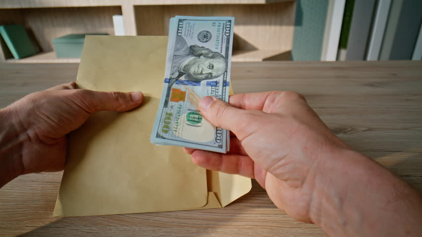 Hands taking money from envelope on wooden office desk closeup. Unknown businessman holding pack of american dollars cash at workplace. Man receiving not official salary. Corruption and shadow economy