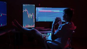 Young stock market trader analyzing real-time charts on multiple computer monitors in dimly lit room while drinking from mug and resting with feet up on desk. Concept of comfort online trading at home - Powered by Shutterstock - Get 15% off with code: PIKWIZARD15