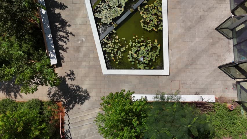 Aerial drone view of a stunning garden with a sparkling swimming pool in the courtyard of a modern building. The lush greenery and stylish design create a serene and luxurious outdoor space.