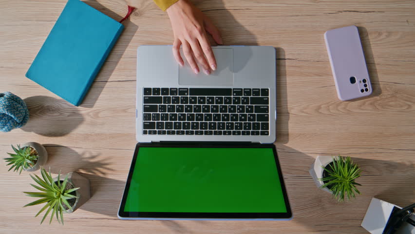 Hand using touchpad mockup laptop in professional indoor workspace closeup top view. Unknown businesswoman surfing internet at green screen computer on wooden desk. Remote work with modern equipment