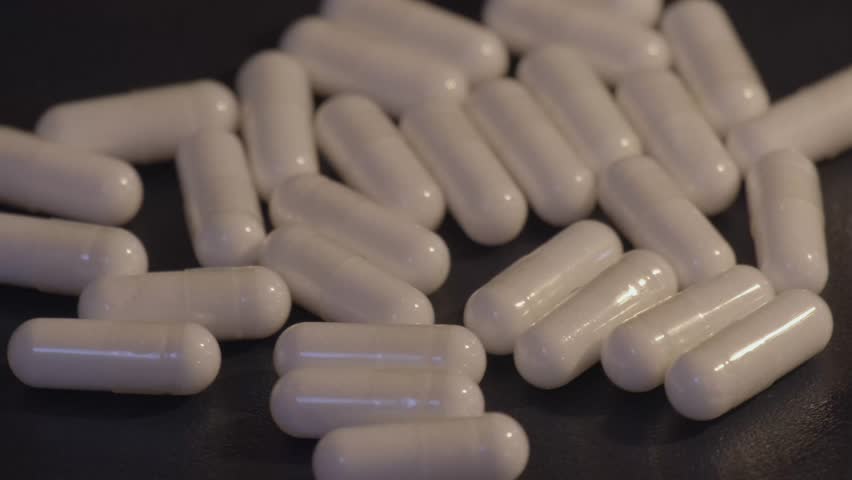 White dietary supplement capsules scattered on a dark background