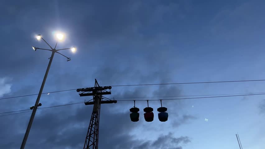 Silhouette of three moving cable car in a blue sky background.