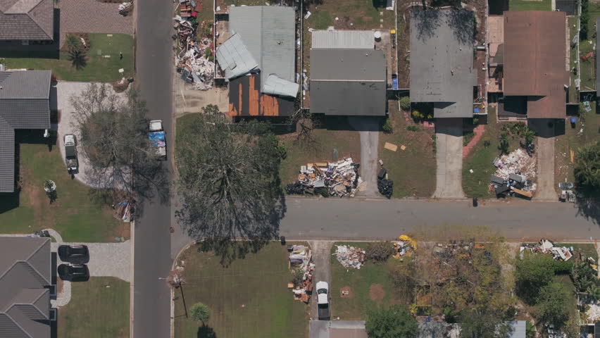 Aerial top-down shot shows rows of houses in St. Petersburg Florida neighborhood with varying degrees of destruction, from piles of trash and debris to roof damage in the wake of Hurricane Milton.