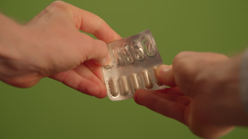 Hands Holding a Blister Pack of Medication Against a Calm Green Background, Promoting Health