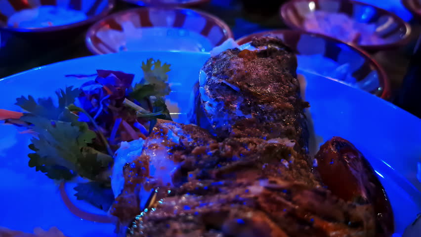 A beautifully arranged seafood plate is enhanced with a rich dressing that is carefully drizzled over it. Fresh garnishes complement the dish, adding color and texture in a dimly lit setting.