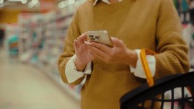 Person is browsing a busy supermarket aisle with a shopping basket in hand, checking items on their smartphone for grocery shopping and planning their purchases. - Powered by Shutterstock - Get 15% off with code: PIKWIZARD15
