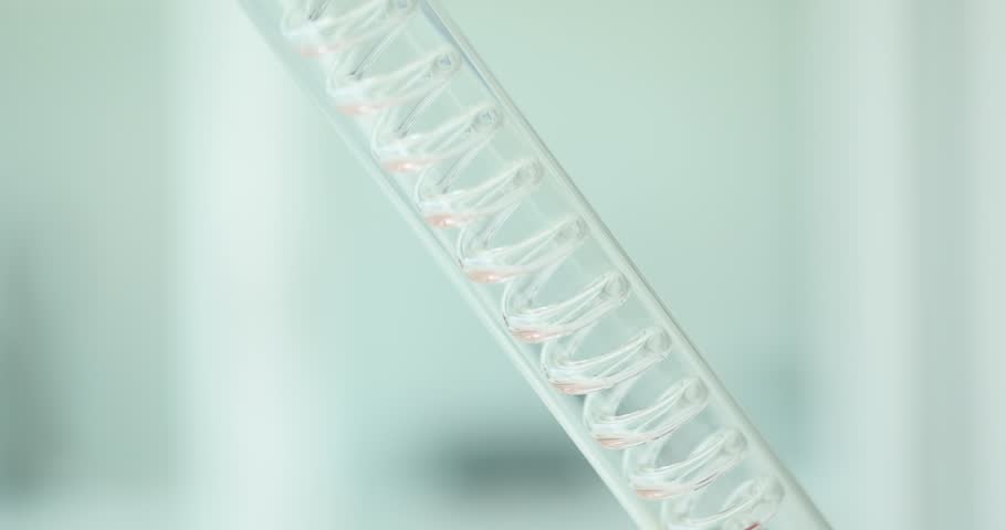 Liquid flows through spiral glass tube in sterile laboratory. Red chemical solution runs in specialized glassware for scientific research