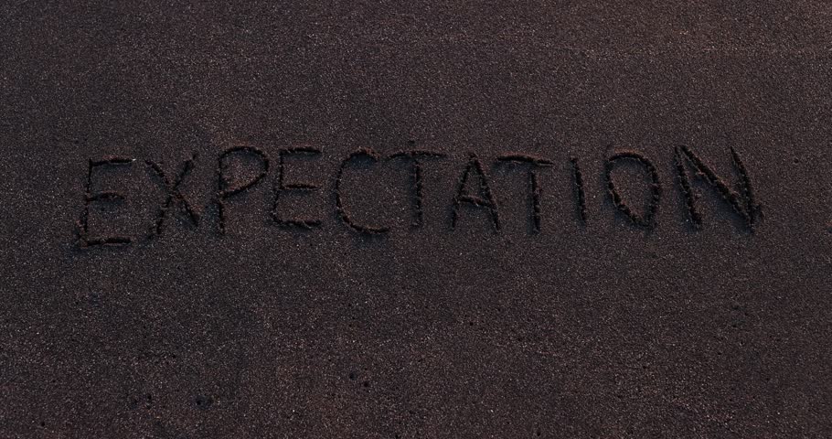 White foam of sea begins to erase letters of word EXPECTATION. Word EXPECTATION carefully written on smooth wet sand. Waves remove inscription