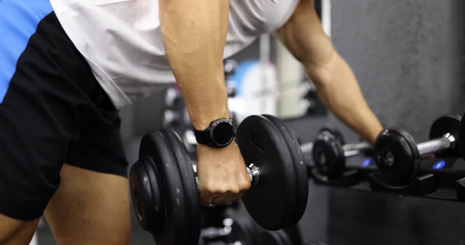 Man bodybuilder takes dumbbell exercising in sports gym. Male lifts weights during training increasing muscle size for bodybuilding purposes