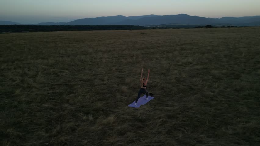 Woman doing yoga in a vast field at sunset. Aerial view showcasing tranquility and fitness in nature. Perfect for wellness, healthy lifestyle, and outdoor activity themes.