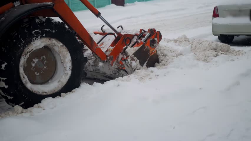 A tractor with a bucket removes snowdrifts in the city, close-up, slow motion, industry