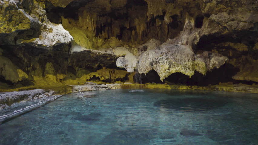Serene natural pool within a cave, surrounded by limestone formations. Water gently cascades from above, creating a calm, tranquil scene.