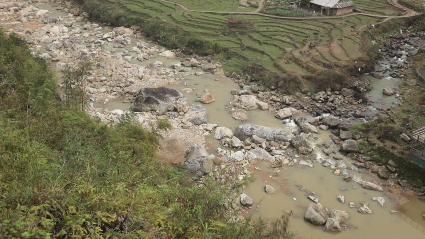 River flowing through terraced rice fields and scattered houses in Sa Pa, Vietnam, on a cloudy day