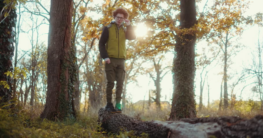 Teen boy crosses a fallen tree while hiking through a forest