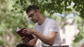 Young man sits on bench in park and reads notes in his notebook. Education, work, plans, ideas, schedule. Man in white t-shirt. - Powered by Shutterstock - Get 15% off with code: PIKWIZARD15
