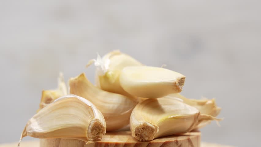 A pile of garlic cloves on a wooden cutting board. The garlic is fresh and ready to be used in cooking. Garlic rotates on wooden background.