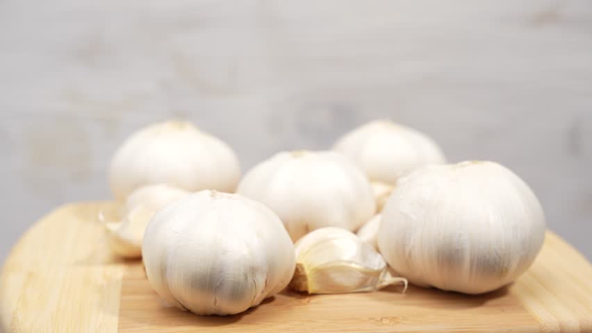 A bunch of garlic cloves are sitting on a wooden cutting board. The garlic is white and he is fresh. Concept of freshness and naturalness. Garlic rotates on wooden background.