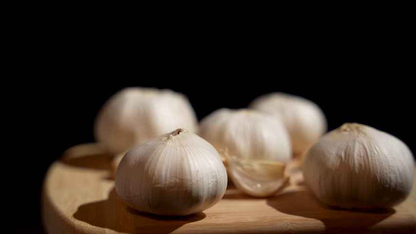 A bunch of garlic cloves rotate on a wooden cutting board. The garlic is fresh and unpeeled, and the image conveys a feeling of freshness and naturalness.