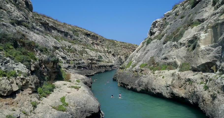 AERIAL: Peole swimming inside Wied il-Ghasri bay. Gozo island, Malta.