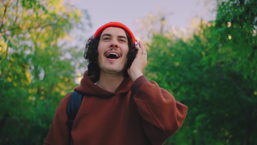 A lively man walks through a sunlit park, music filling his headphones. His dance moves bring a joyful vibe, adding life to the tranquil natural setting