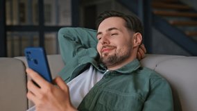 Closeup guy messaging smartphone lying at light couch. Relaxed happy man typing message in social media watching funny content online at weekend. Smiling freelancer using mobile phone at living room - Powered by Shutterstock - Get 15% off with code: PIKWIZARD15