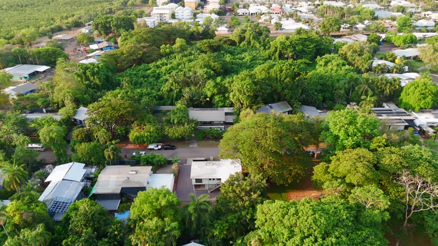 Aerial drone pullback of green suburban neighborhood with tree-lined streets, perfect for real estate showcasing in tropical area