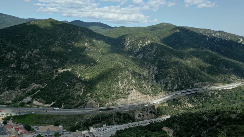Witness the stunning landscape where a highway weaves through lush mountain valleys under a vibrant sky during late afternoon. Nature