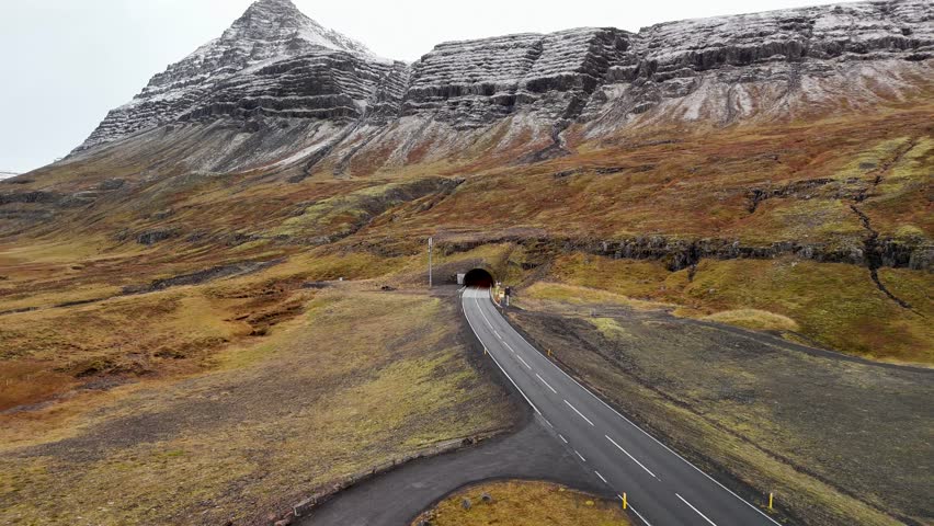 Aerial view of driving bus into tunnel of icy mountain Iceland. Mossy landscape on Iceland in autumn season. Wide shot.