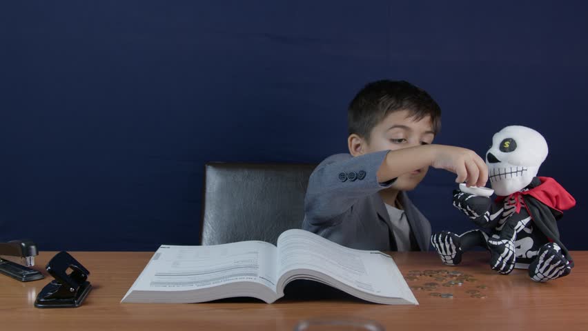 A child reads a financial book near his skeleton money bank. puts coin in the money bank. High quality 4k footage
