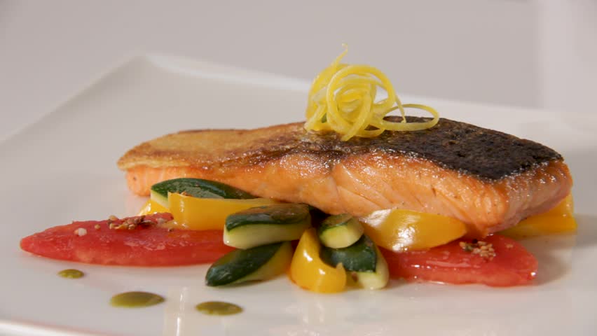 A chef garnishes a beautifully plated grilled salmon dish with fresh vegetables and herbs