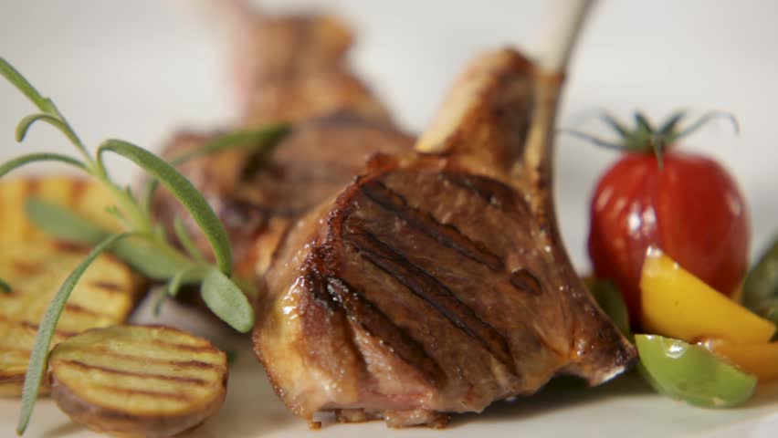 Juicy lamb chops with rosemary, grilled vegetables, and rich sauce being poured over