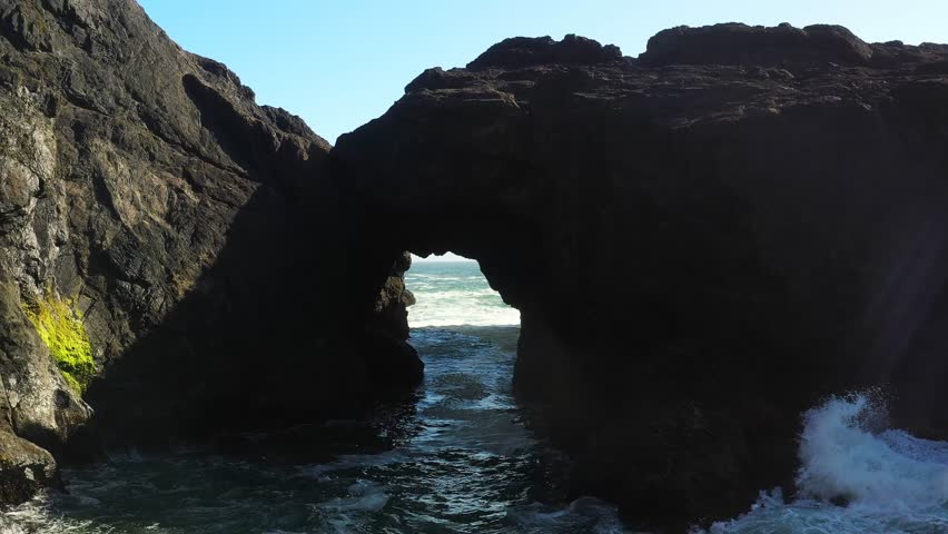 Scenic aerial view of cliff side rocks forming an arch and ocean waves crashing on the shore of Pacific Northwest, Oregon.