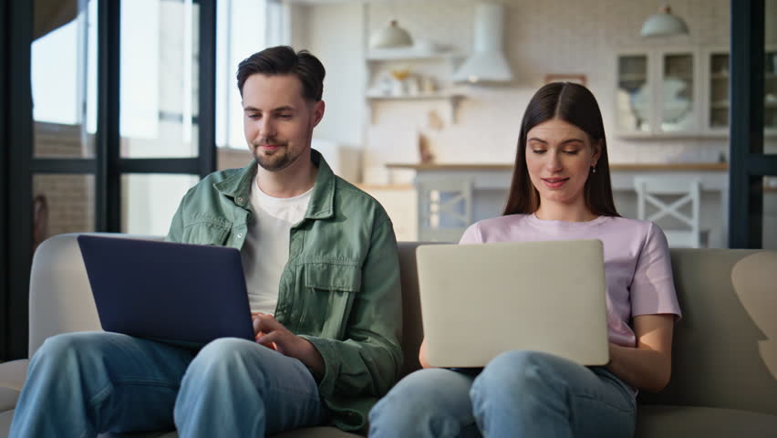 Working couple discussing laptop screen talking together at couch closeup. Busy lovers texting computers at home. Relaxed man looking wife asking question at flat. Young spouses lifestyle concept