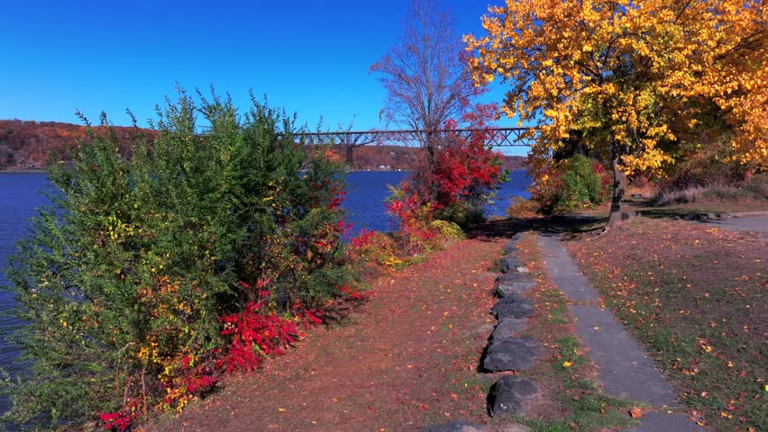 A low altitude drone view in Kaal Rock Park and over the Hudson River on a sunny day during the colorful fall season. The camera dolly in, pan left and tilt up, revealing the mid Hudson Bridge.